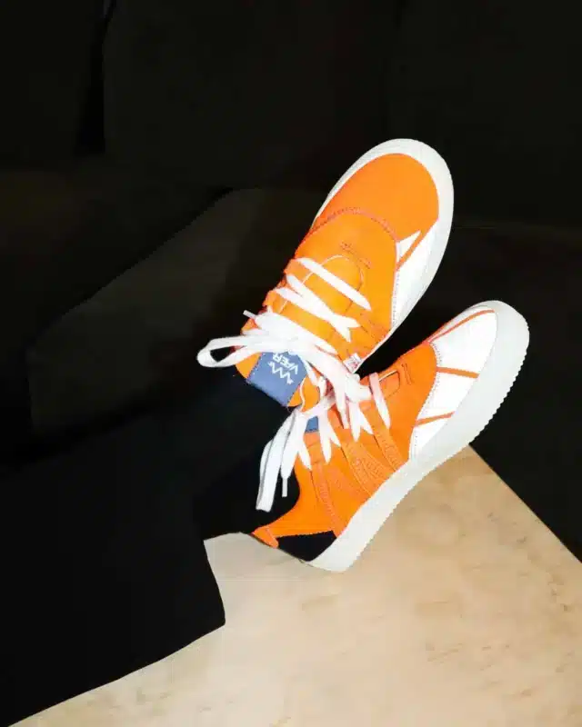 A worn pair of VAER Phoenix sneakers in orange, cut from upcycled workwear textile, with white soles.